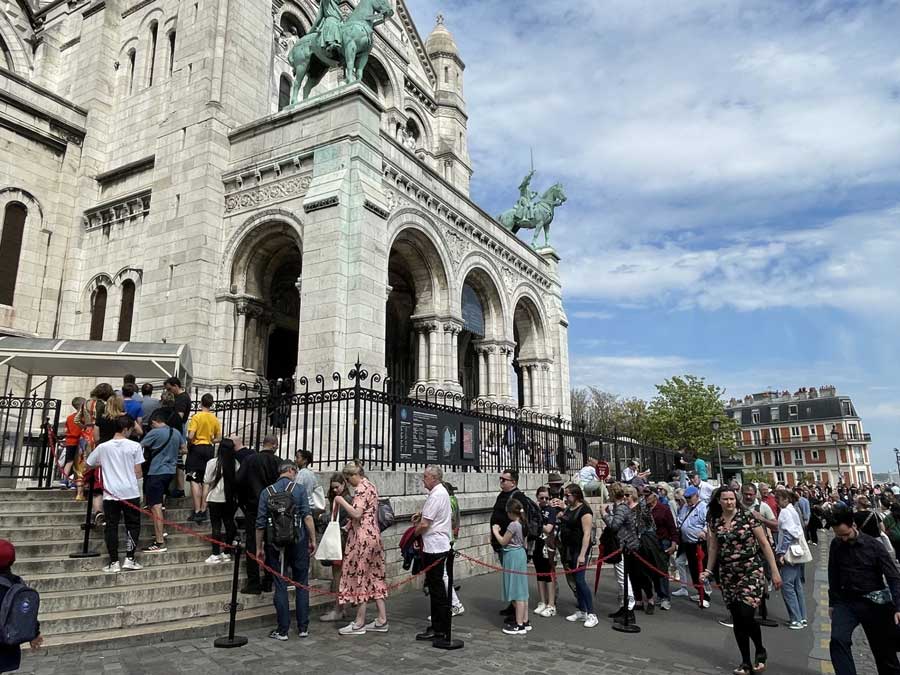 Visitors waiting in line to enter Sacré-Cœur in Paris. Comfortable shoes and respectful clothing are useful here, especially because you may be standing, walking uphill, and visiting a religious site.
